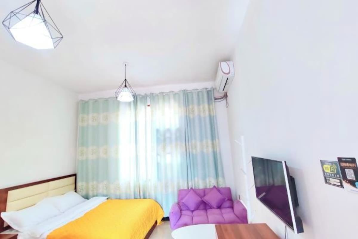 A hotel room with a bed, a purple armchair, a TV, and a ceiling light.