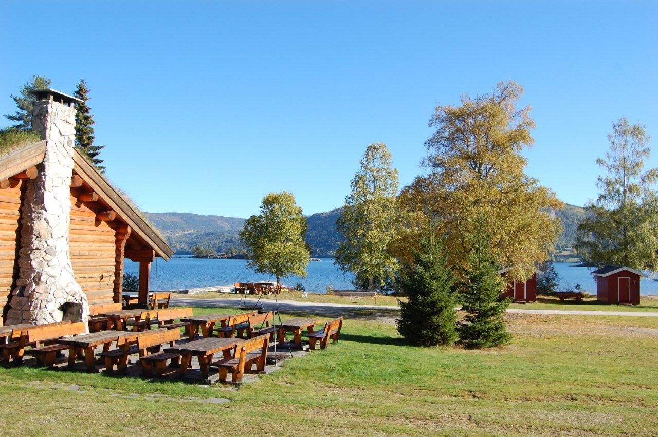 Eine Lodge mit Kamin aus Stein, Holzbänken und Picknicktischen am See.