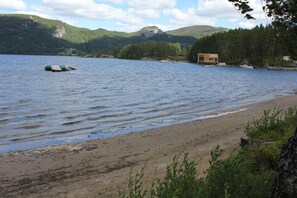 Vista de un lago con playa de arena, una cabaña de madera y un boya flotando.