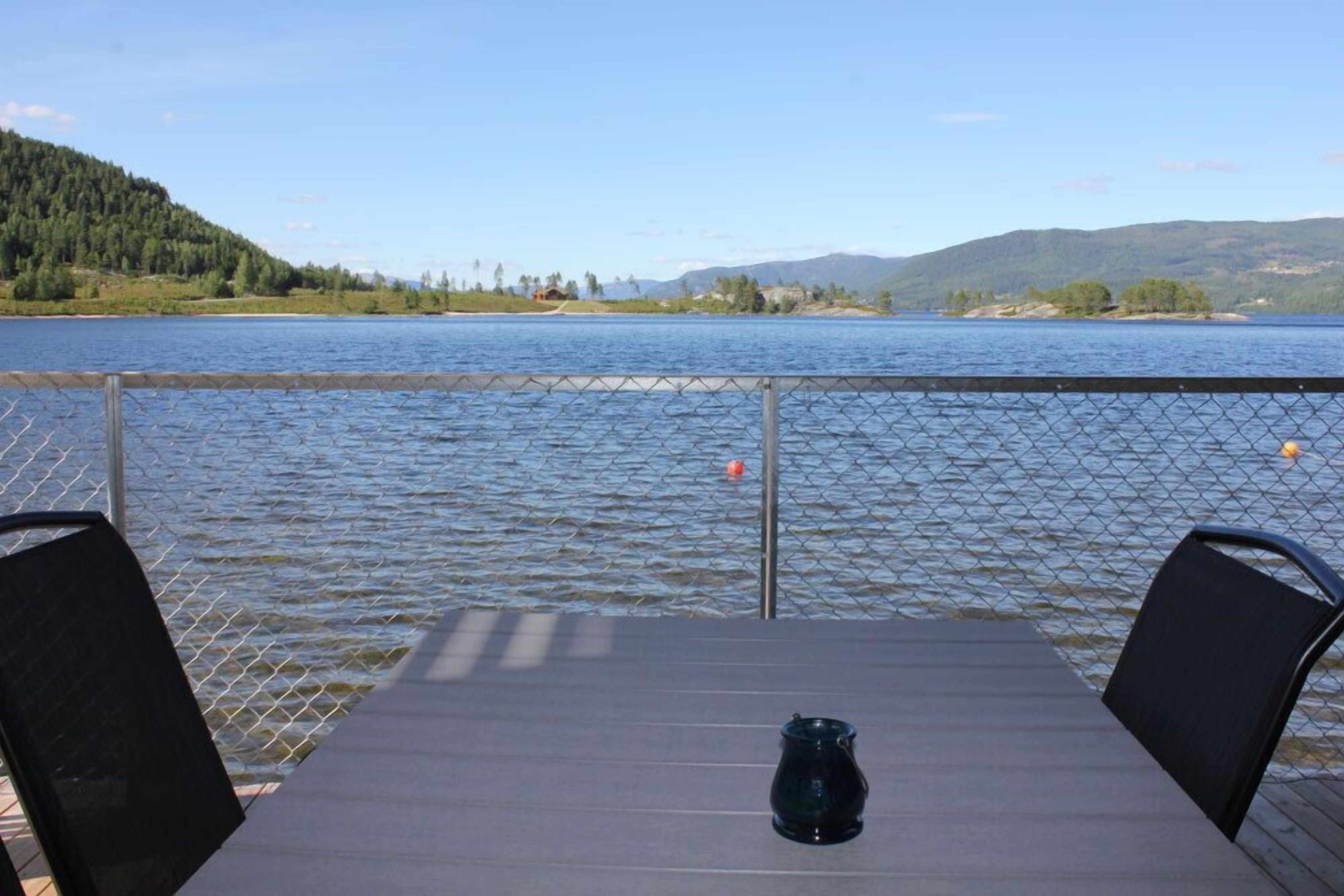 Una mesa con sillas en una terraza con vista a un lago, con una cerca al frente.