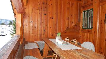 Une cabane en bois avec une table et des bancs en bois, une fenêtre avec des volets verts, et une vue sur un parking et des montagnes.