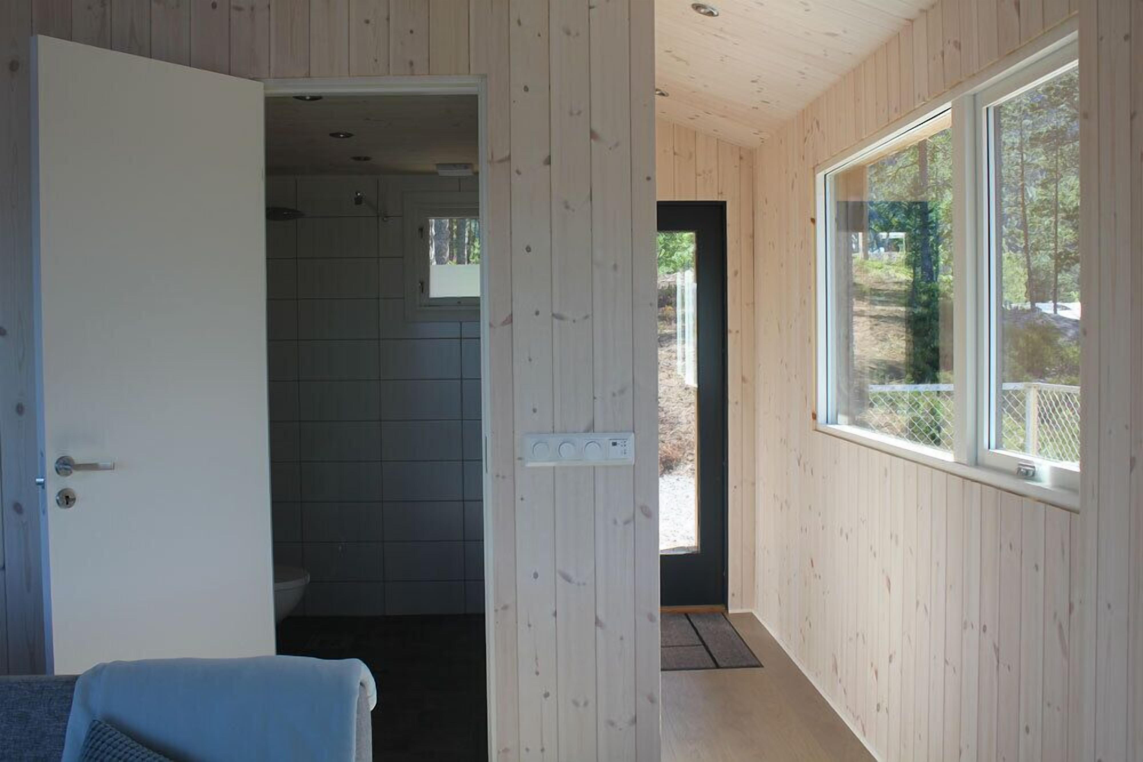 A room with wooden walls, a large window, and a door leading to a bathroom.