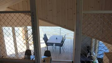 Una terraza de madera con una mesa y sillas, vista al agua y una cerca de malla metálica.