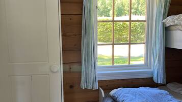 Una habitación tipo cabaña con interior de madera, una ventana con cortinas, una cama y una puerta.