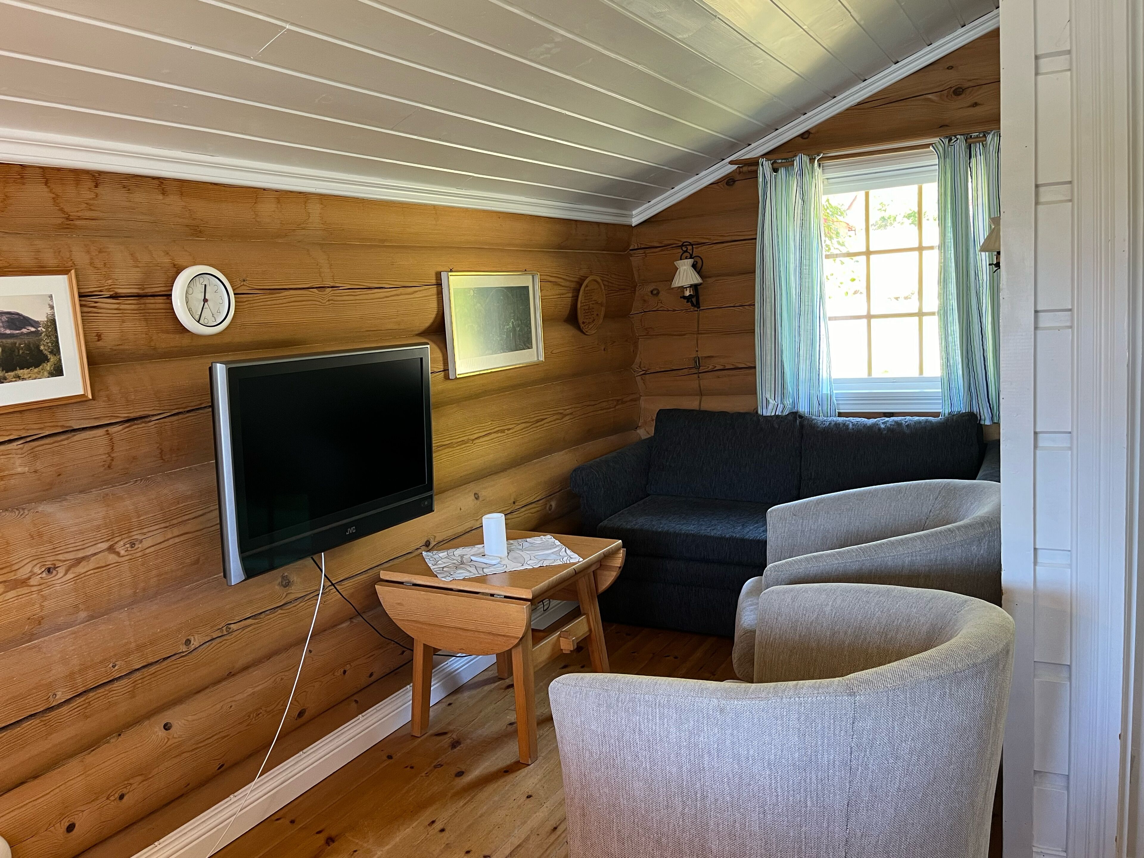 A cozy cabin interior with a wooden interior, a flat-screen TV, a sofa, and a small table with a lamp.