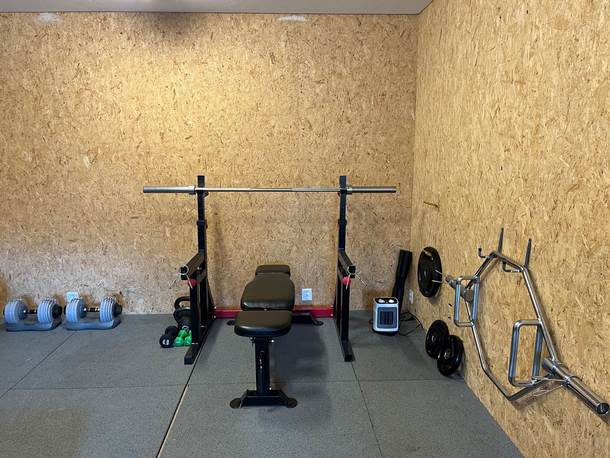 A home gym with a bench press, barbell, weight plates, dumbbells, and a pull-up bar.
