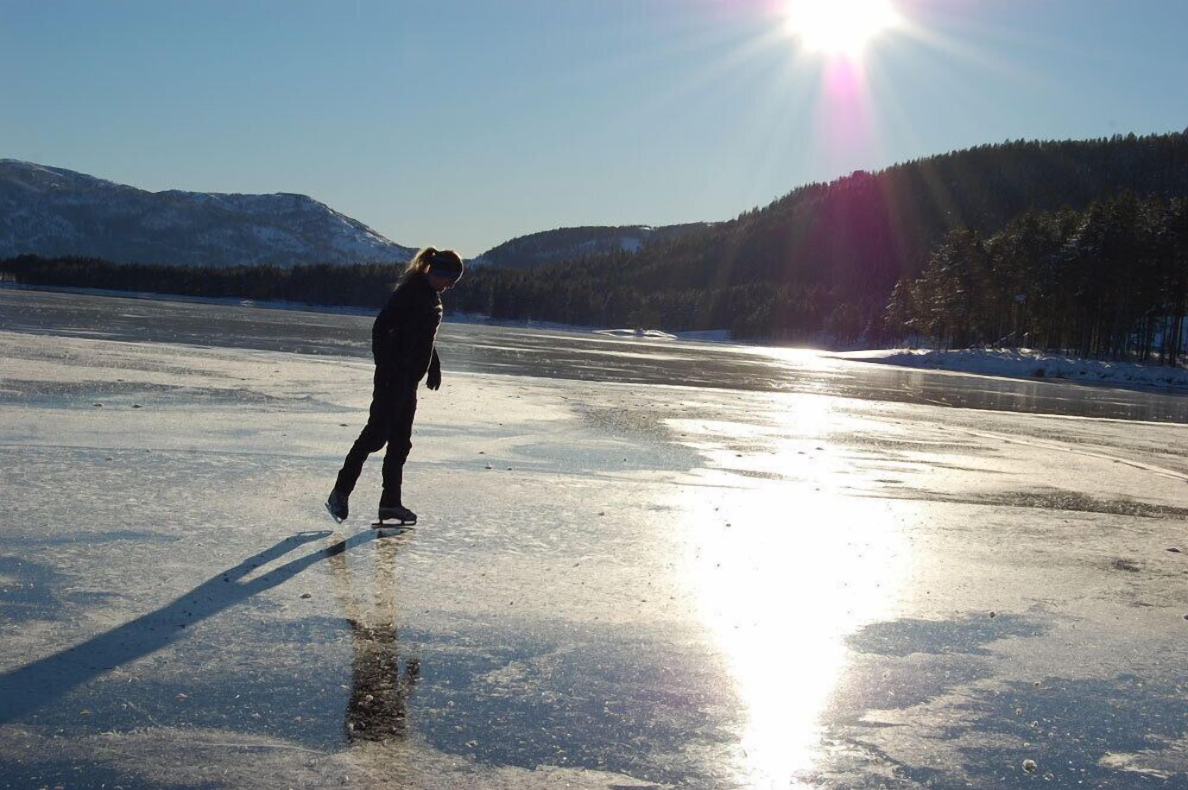 A person ice skating on a frozen lake with mountains in the background.