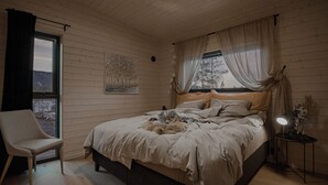 A bedroom with a bed, a chair, a bedside table, and a window with curtains.