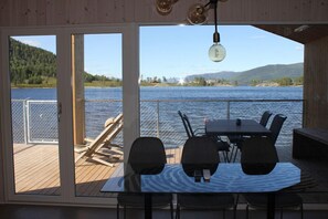 A wooden deck with a table and chairs overlooking a lake, with a view of hills and a fence in the background. - Nisser Hyttegrend Og Camping (Nissedal)