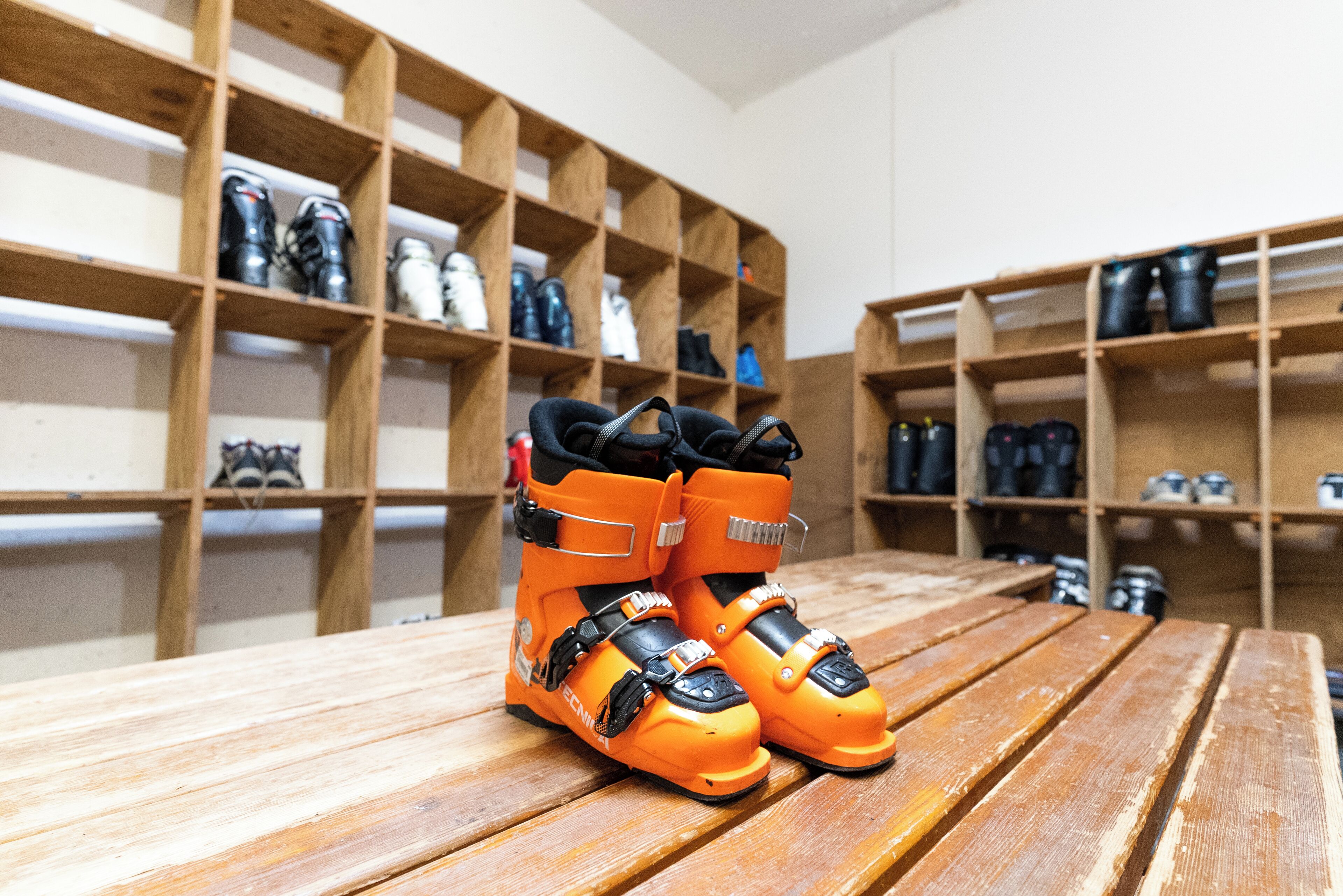 Een paar oranje skischoenen op een houten tafel in een kamer met houten planken vol diverse spullen.