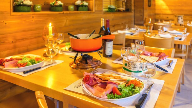 Un interior de madera con mesas dispuestas para comer, con platos de comida, copas de vino y una vela.
