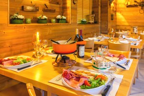 A wooden interior with tables set for dining, featuring plates of food, wine glasses, and a candle. - Azureva Métabief (Métabief)