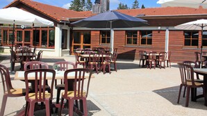 Un patio al aire libre con mesas y sillas de madera, sombrillas y un edificio con techo de tejas rojas.