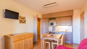 Un espacio habitable compacto con kitchenette, comedor y televisor montado en la pared.