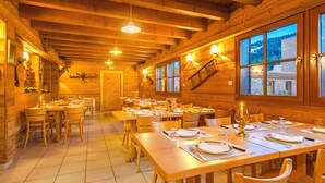 Un interior de madera con varias mesas y sillas de comedor, vigas de madera en el techo y grandes ventanales con vistas al exterior.