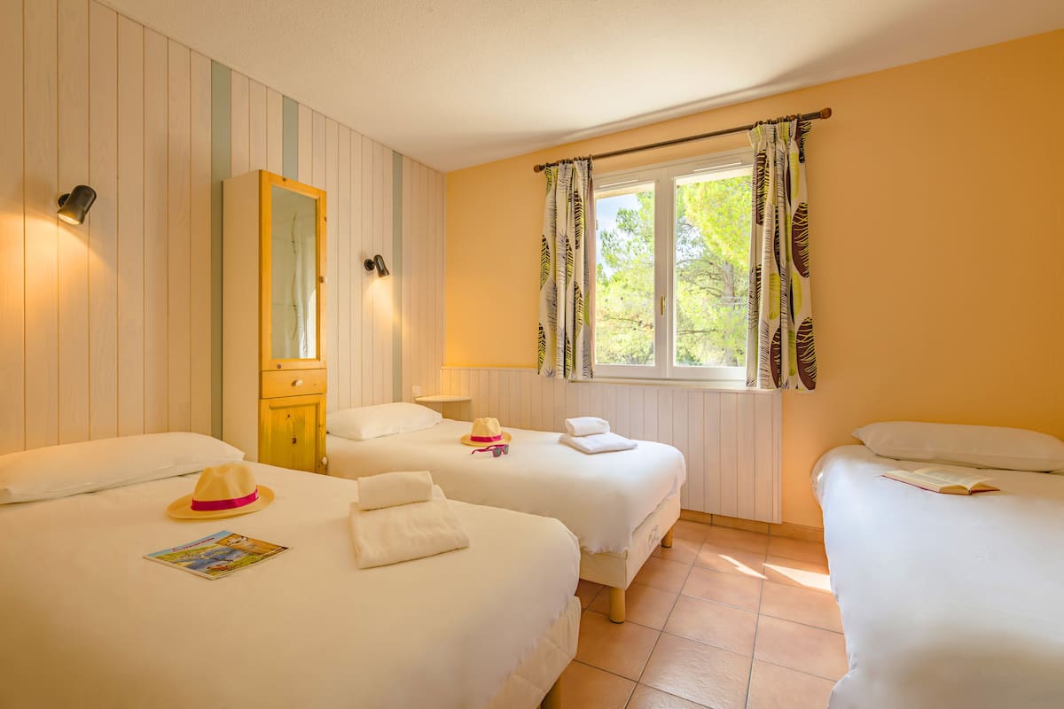 A hotel room with two beds, a mirror, a window with curtains, and a lamp.