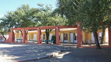Un edificio con techo rojo y puertas blancas, con mesas al aire libre y un espacio cubierto.