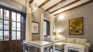 A modern living room with a dining area, featuring exposed wooden beams, a sofa, a table, and chairs. - Mon Suites San Nicolas (Valencia)