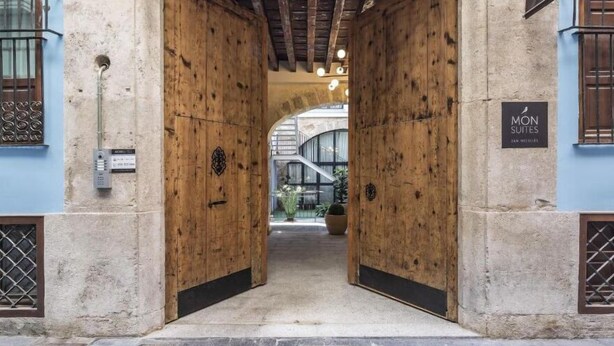 A hotel entrance with wooden doors, a stone wall, and a sign for 'MON SUITES'. - Mon Suites San Nicolas (Valencia)