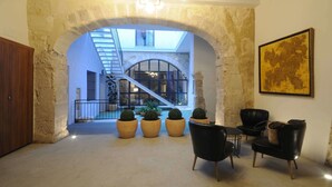 An interior with a stone archway leading to a staircase, potted plants, and black leather chairs. - Mon Suites San Nicolas (Valencia)