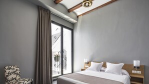 A modern hotel room with a large bed, a chair, a nightstand, and a view of the outside. - Mon Suites San Nicolas (Valencia)