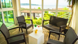 Ein Balkon mit Korbstühlen und einem Tisch, der einen malerischen Blick auf ein Gewässer und viel Grün freigibt.