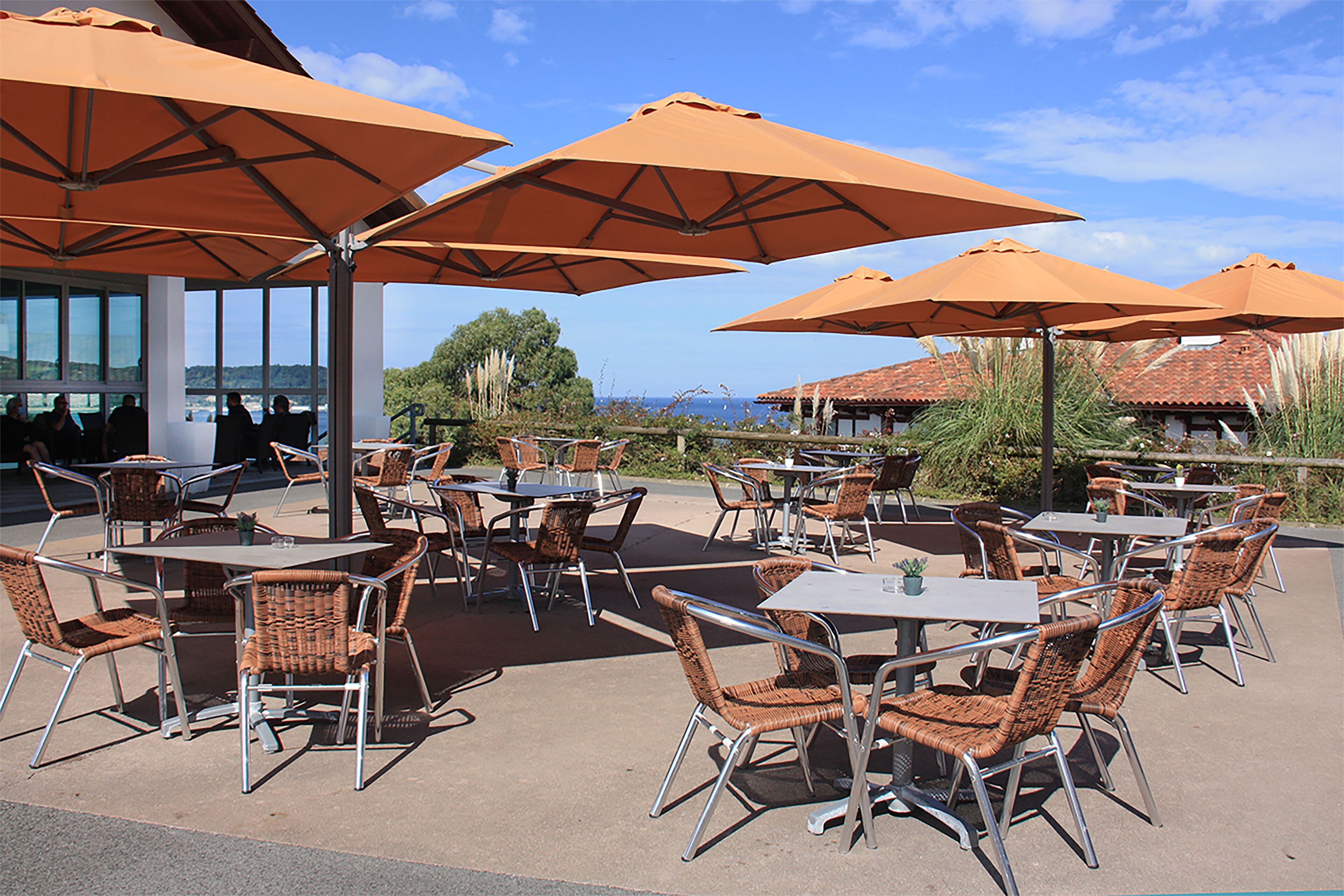 Une terrasse extérieure avec des tables et des chaises, de grands parasols et une vue sur l’océan.