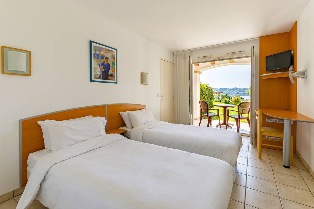 Habitación de hotel con dos camas, televisión y balcón con vistas.