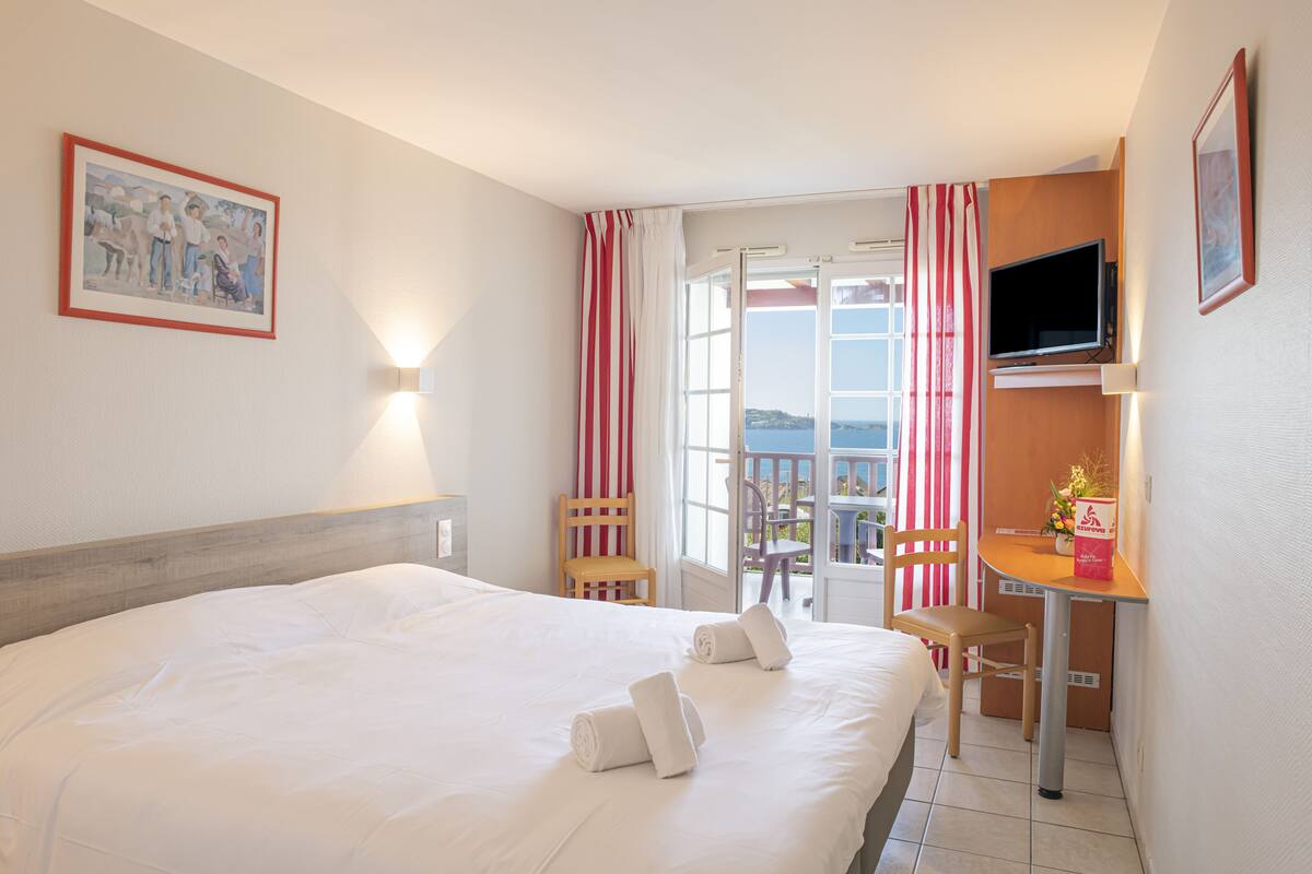 Una habitación de hotel con cama, escritorio con silla, televisor y ventana con cortinas.