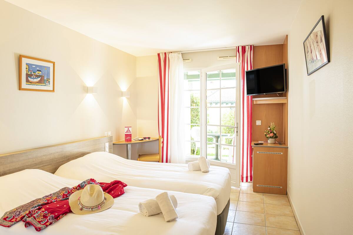 Habitación de hotel con dos camas, televisor, escritorio y ventana con cortinas.