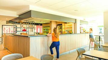 L'intérieur d'un café moderne, avec un comptoir en bois, un espace salon et des panneaux d'affichage où figure le menu.