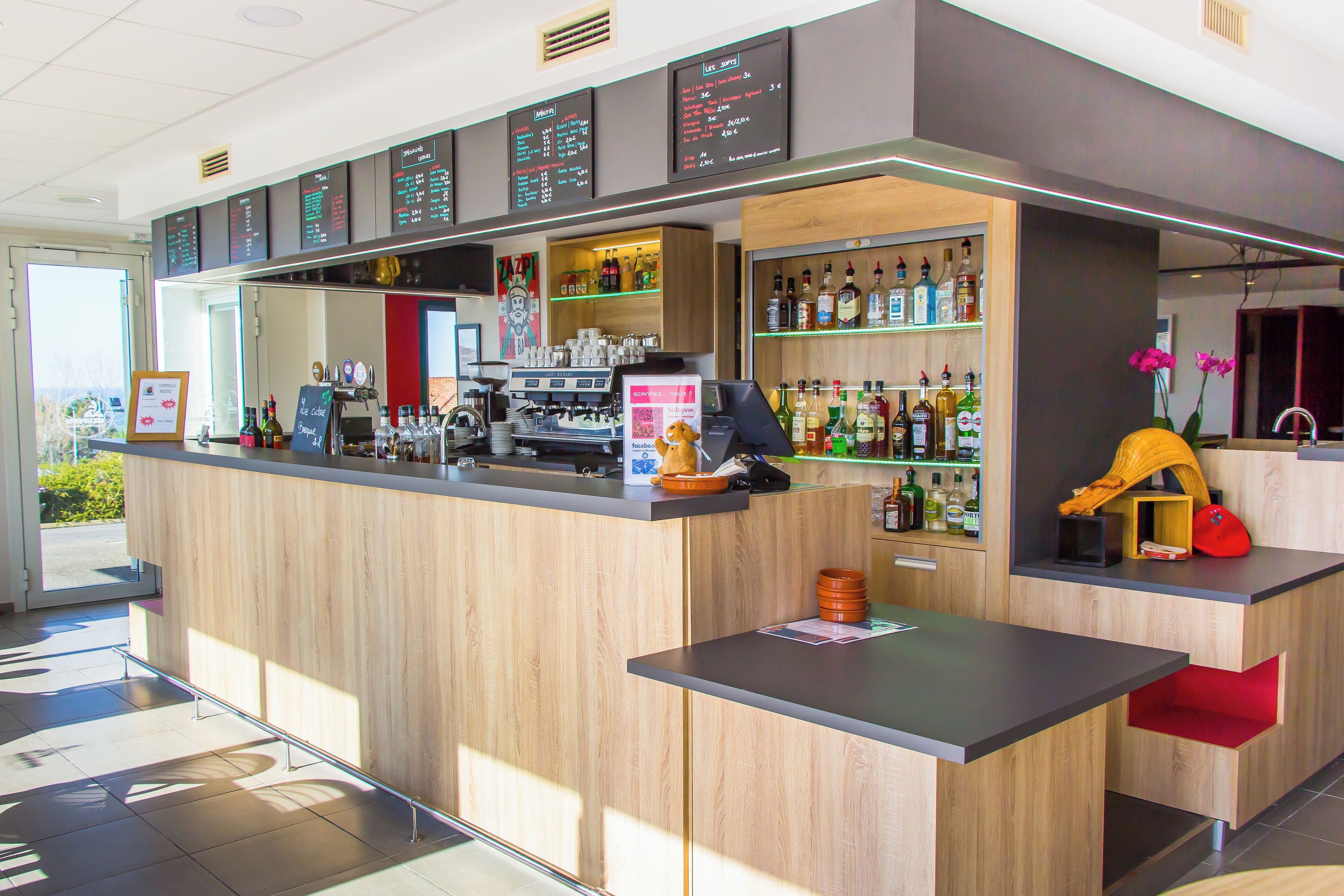 A modern bar area with a wooden counter, a coffee machine, and shelves stocked with various bottles.
