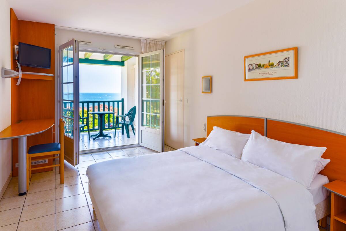 Habitación de hotel con cama, escritorio con silla, televisión y balcón con vista al mar.