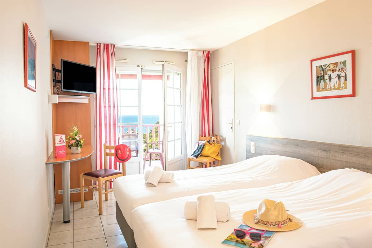 Habitación de hotel con cama, escritorio, silla, televisor y balcón con vista al mar.