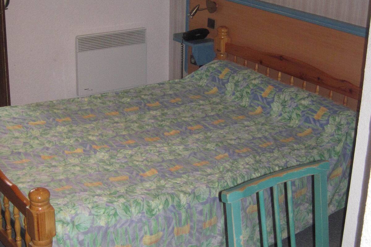 Ein kleines, schlichtes Zimmer mit einem Einzelbett, einem Holzstuhl, einem Schreibtisch und einer Heizung.
