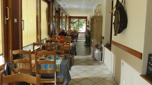 Un long couloir avec des tables et des chaises, des portes en bois et un sol carrelé.