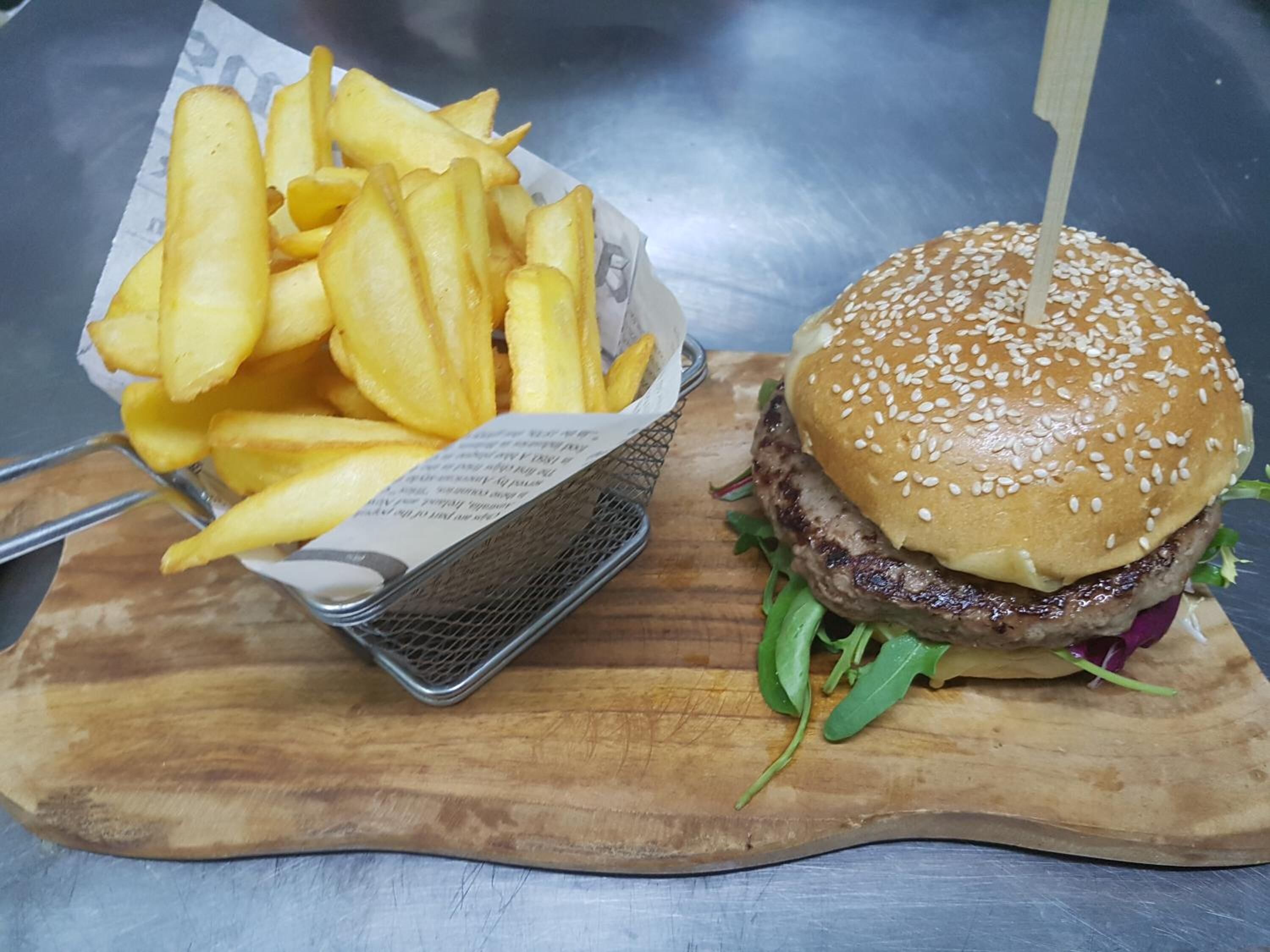 A burger with a sesame seed bun and a side of French fries on a wooden cutting board.