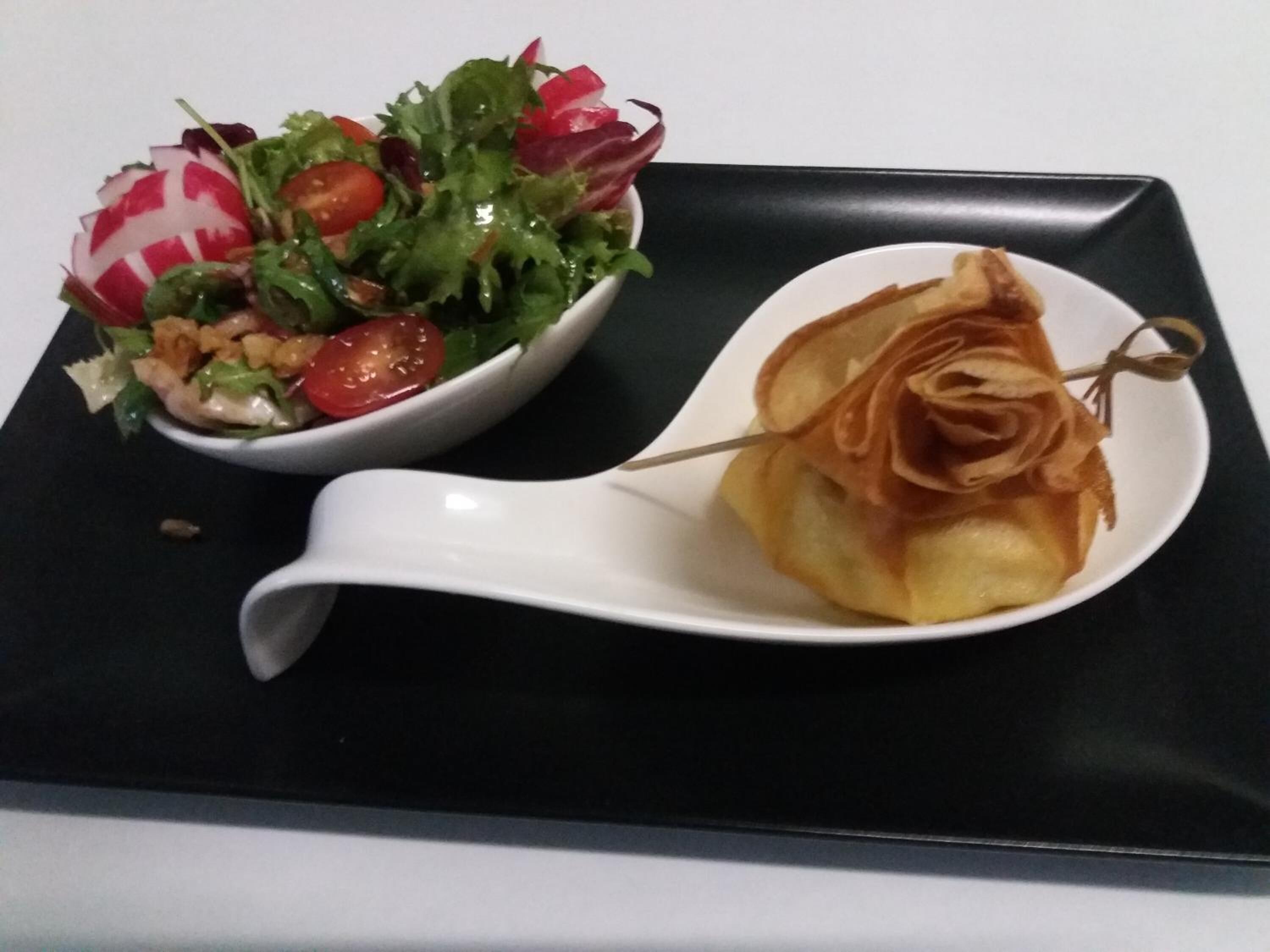 Une assiette blanche contenant une salade et une pâtisserie, le tout posé sur un plateau noir.