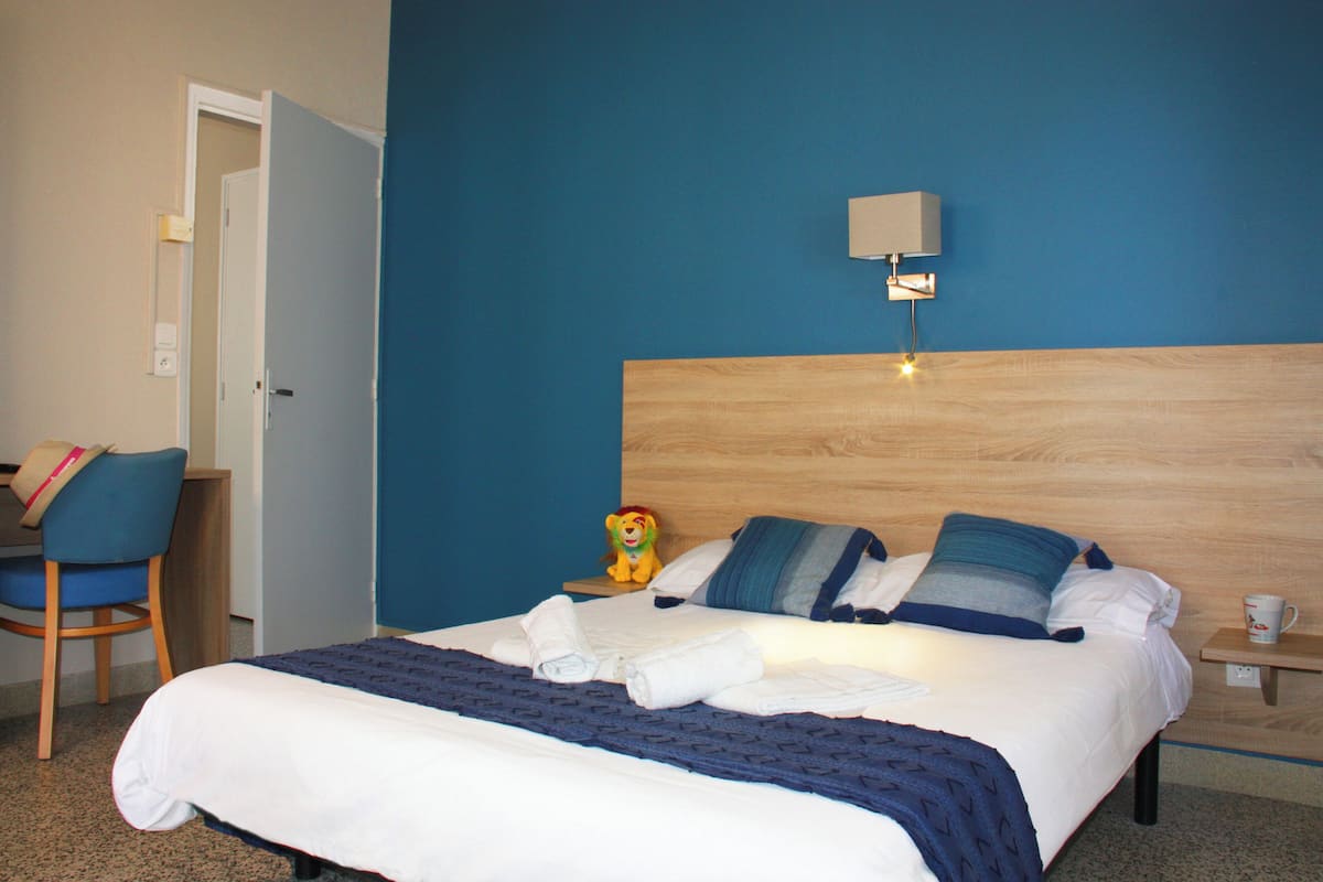 Une chambre d’hôtel comprenant un lit, un bureau, une chaise et une table de chevet avec une lampe.