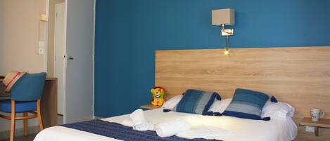 Una habitación de hotel con una cama, un escritorio, una silla y una mesita de noche con lámpara.