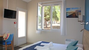 Ett hotellrum med en säng, ett skrivbord, en stol, en tv och ett fönster med utsikt över träd och en solnedgång.