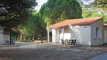 Un pequeño edificio de una sola planta con techo de tejas, un patio cubierto con mesa y sillas, y un letrero que indica que es una casa de huéspedes.