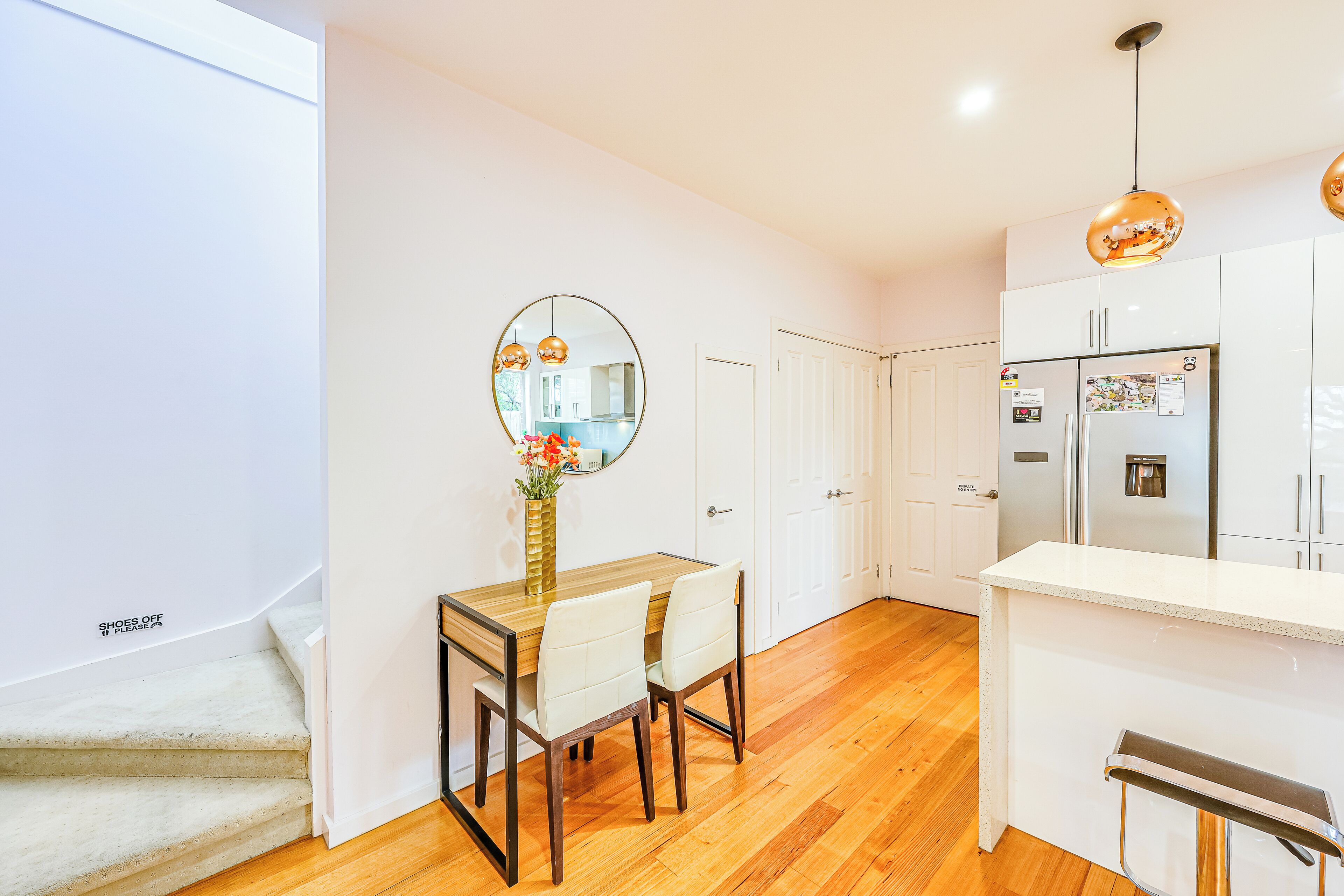 A modern kitchen with white cabinets, a wooden dining table, and a hanging pendant light.