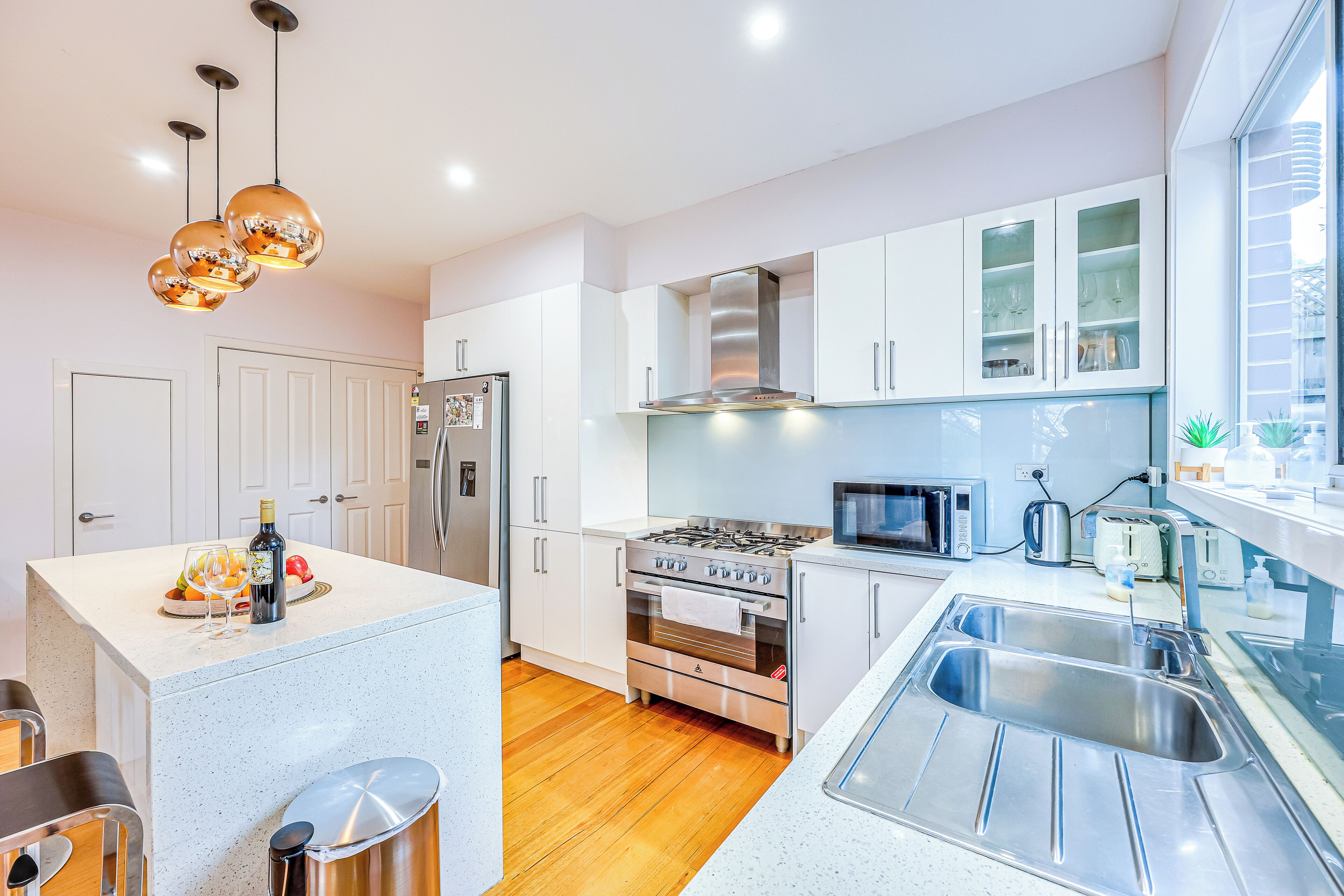 A modern kitchen with white cabinetry, stainless steel appliances, a central island with seating, and pendant lighting.