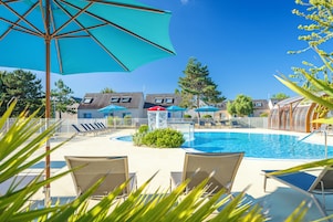 A swimming pool area with lounge chairs and umbrellas, surrounded by buildings and trees.