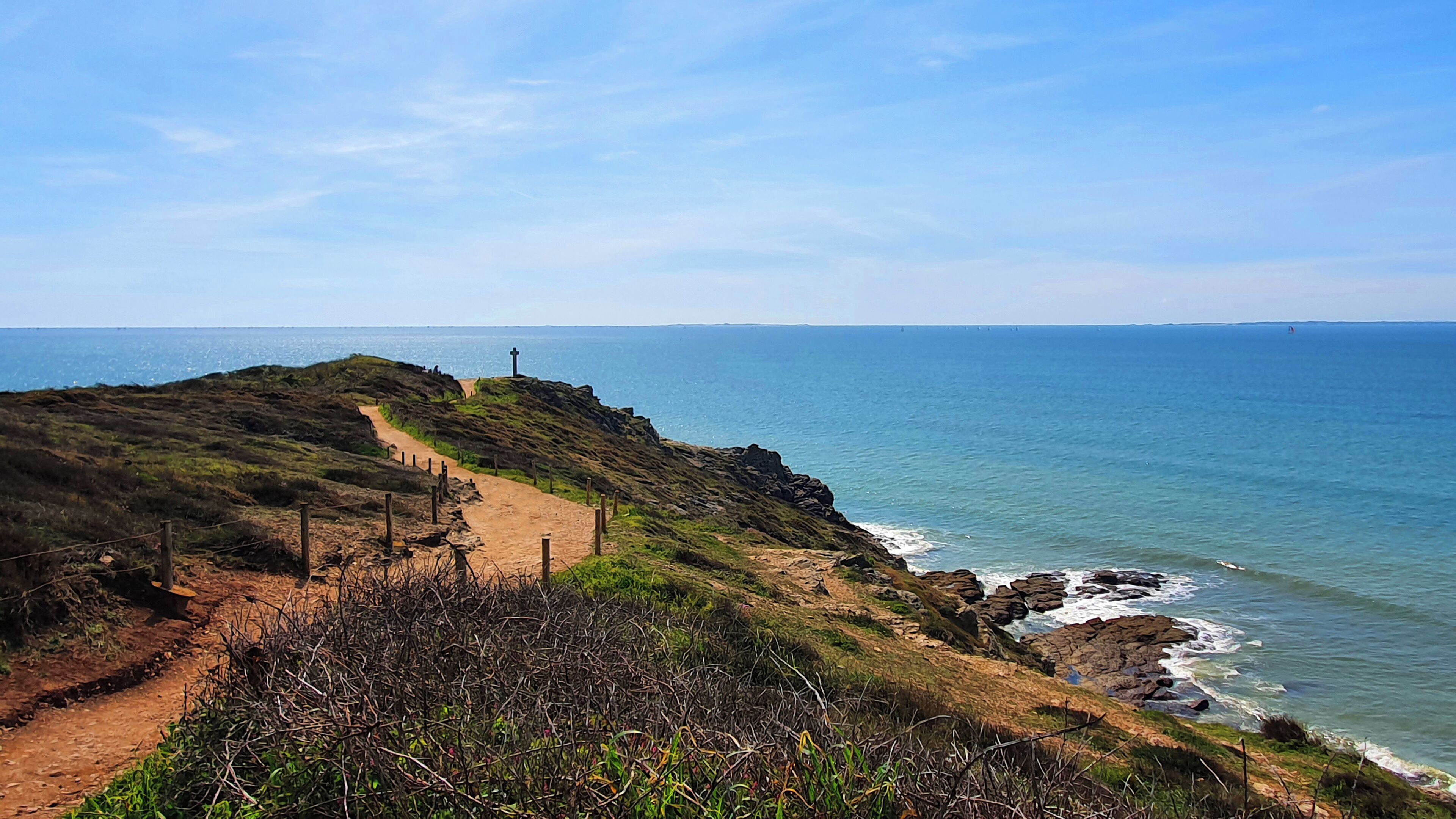 A coastal path with a cross, leading to the sea.