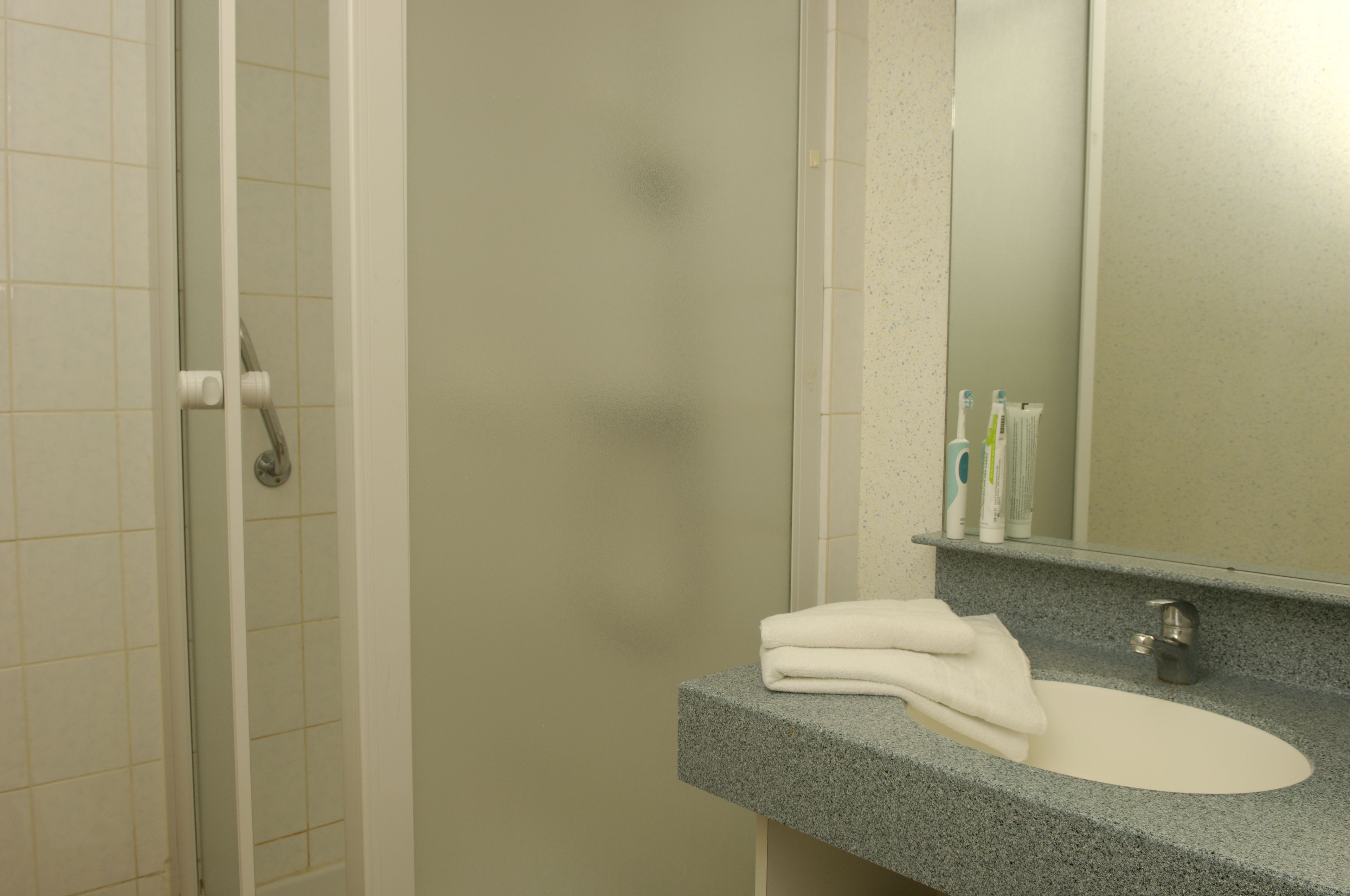 Une salle de bain avec un lavabo blanc, un miroir et un espace douche.