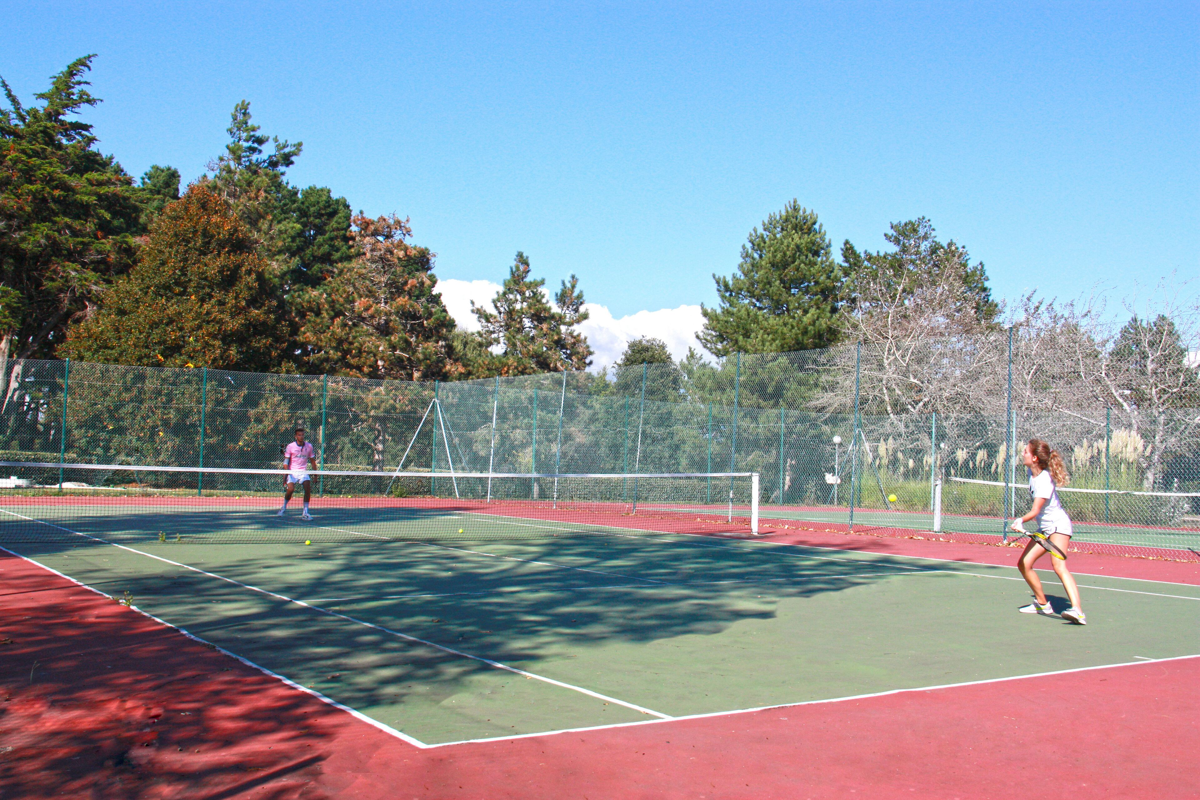 Un campo da tennis con una rete, due giocatori e una recinzione.
