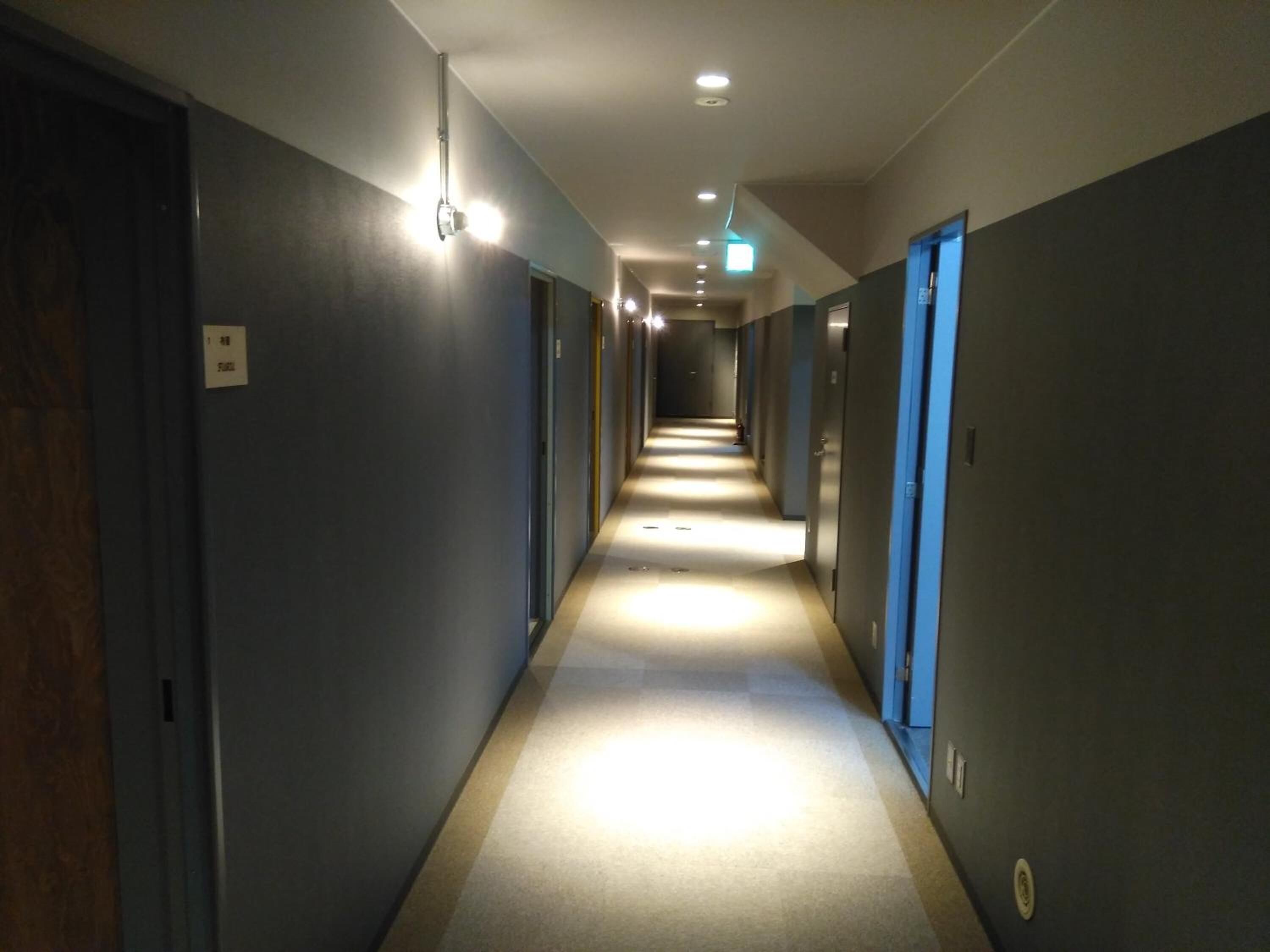 A long, narrow hotel corridor with doors on both sides, recessed lighting, and a carpeted floor.