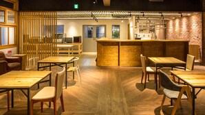 A restaurant with wooden tables and chairs, a brick wall, and a counter. - Mori no Guest House - Hostel (Tenri)